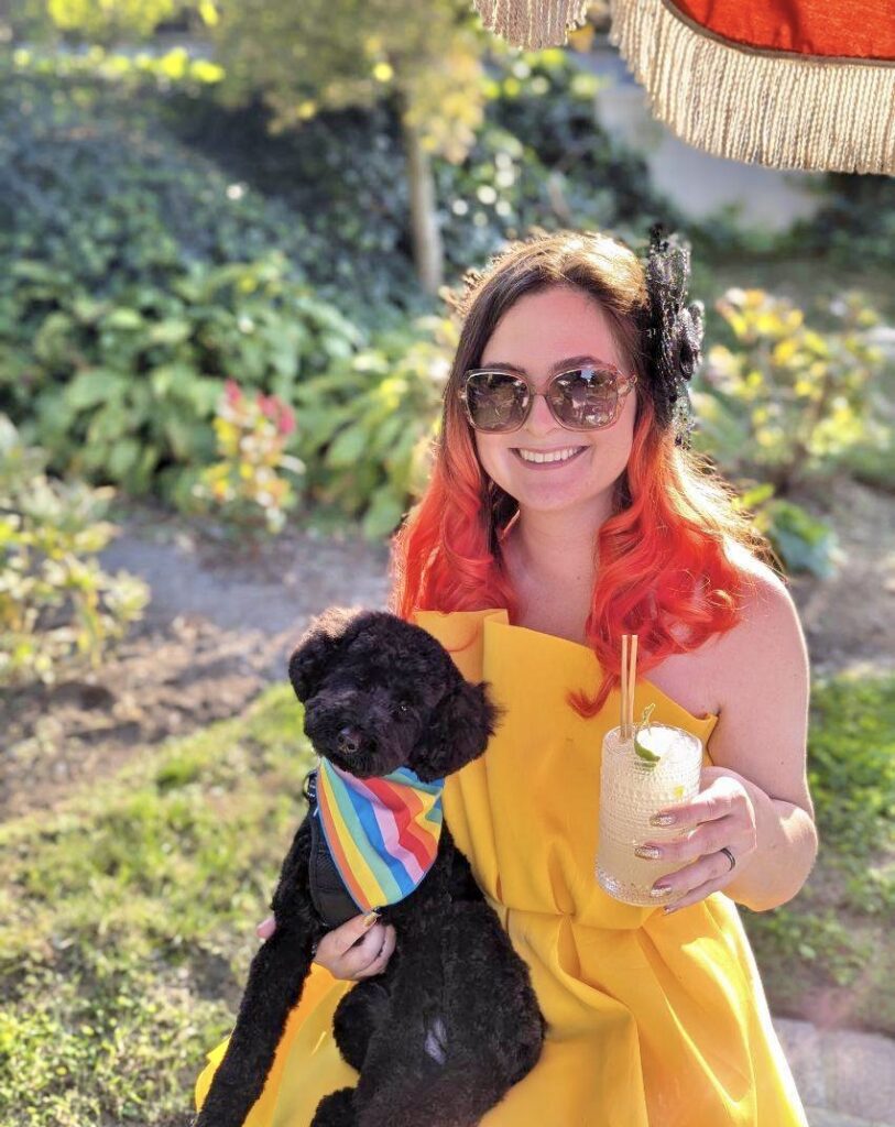 Image of me in a yellow dress holding a black poodle and a virgin margarita.